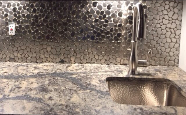 Closeup of the sink area, with metallic pebble mosaics for the backsplash and a rich patterned countertop.